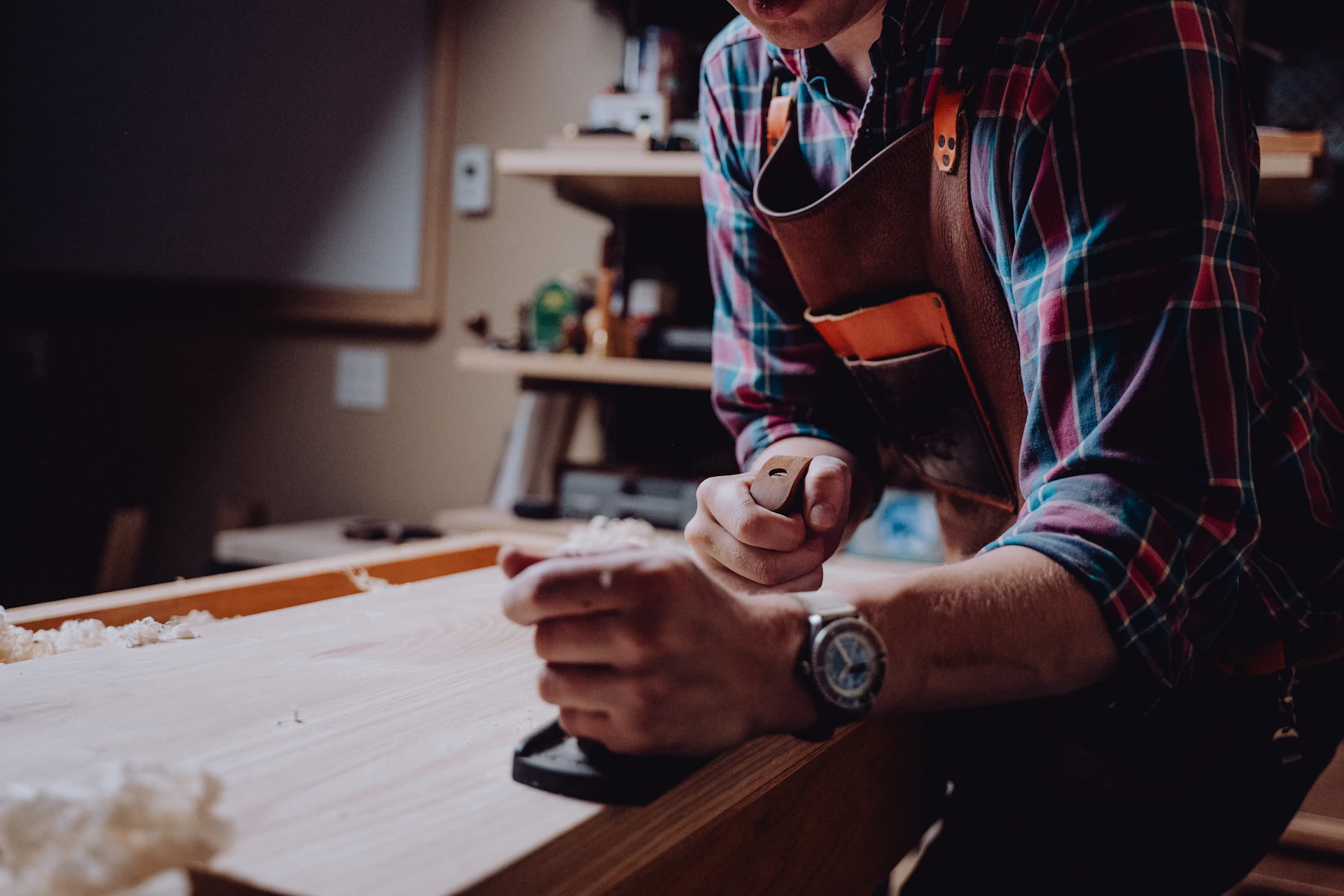 Craftsman working on a timber furniture piece in a workshop, wearing a leather apron